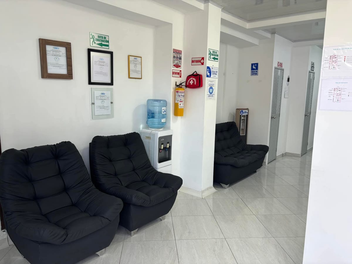 Sala de espera del laboratorio, con sillas, dispensador de agua y los certificados de habilitación enmarcados en la pared.